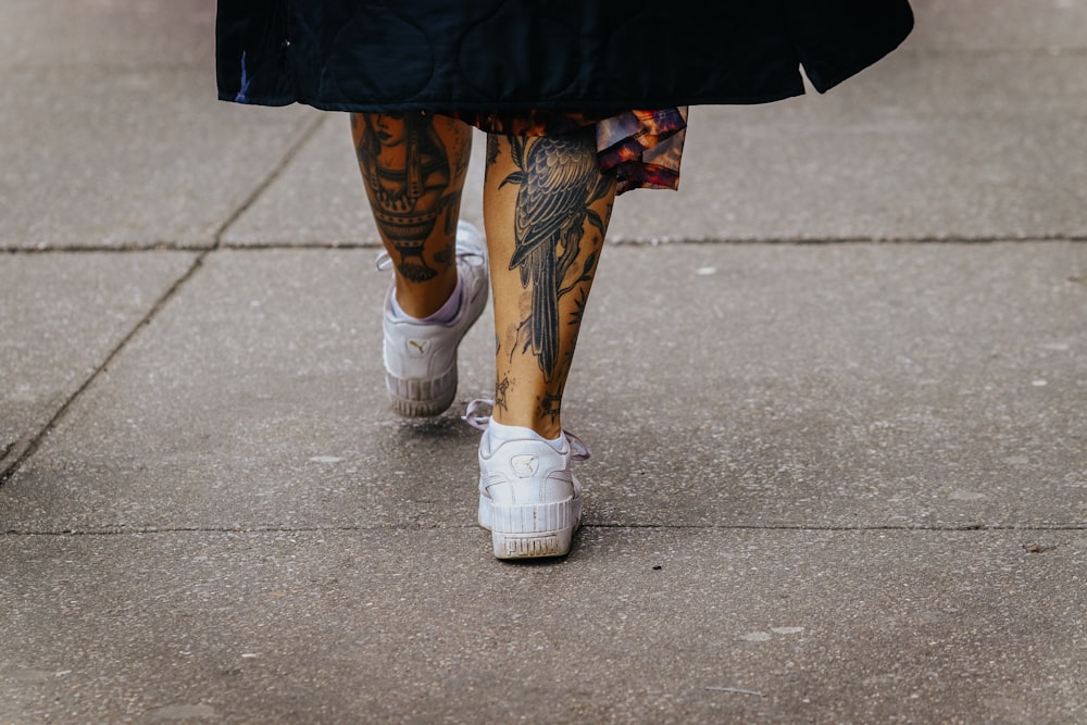 a person with tattoos walking down a sidewalk