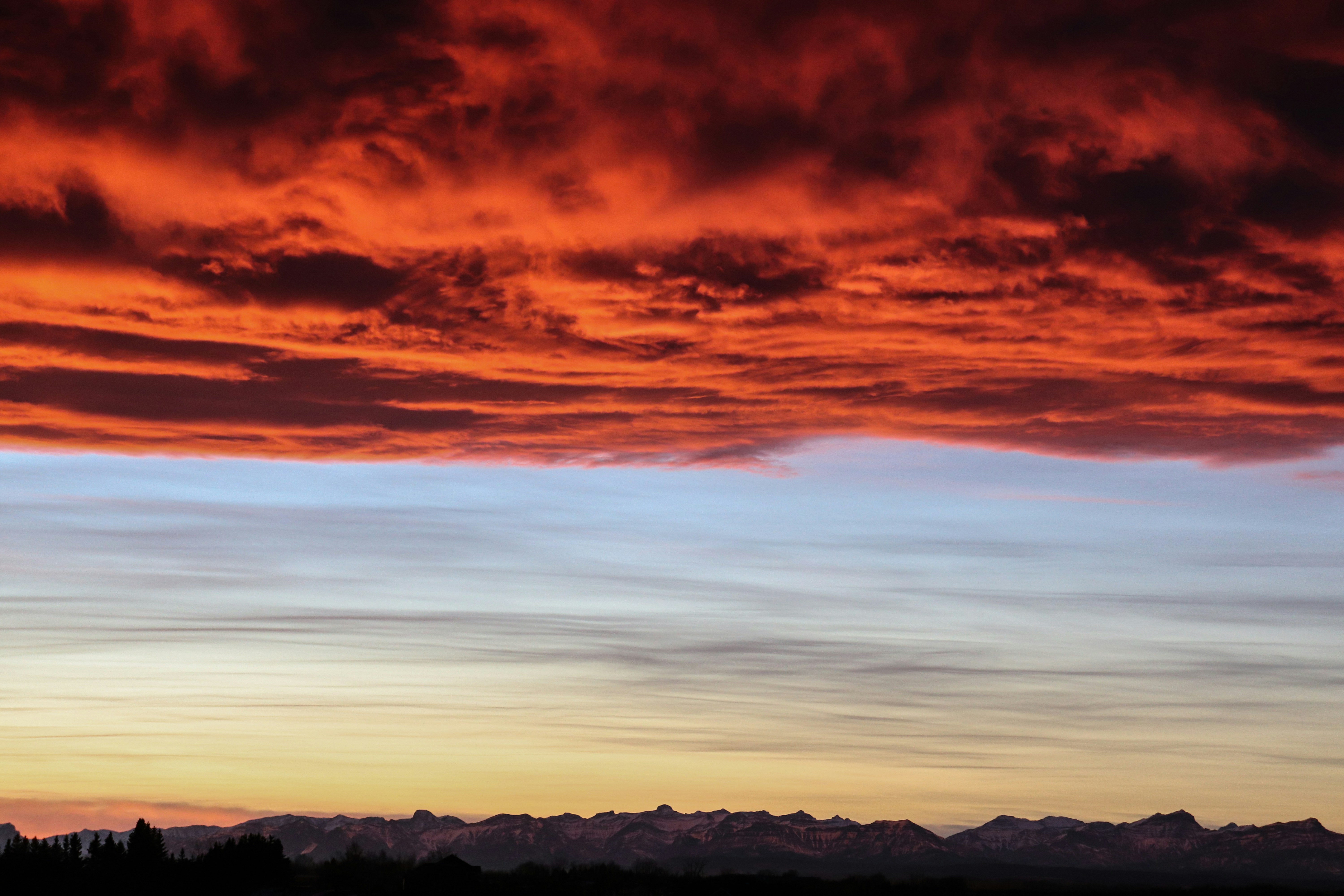 un ciel rouge et bleu avec des nuages et des montagnes en arrière-plan