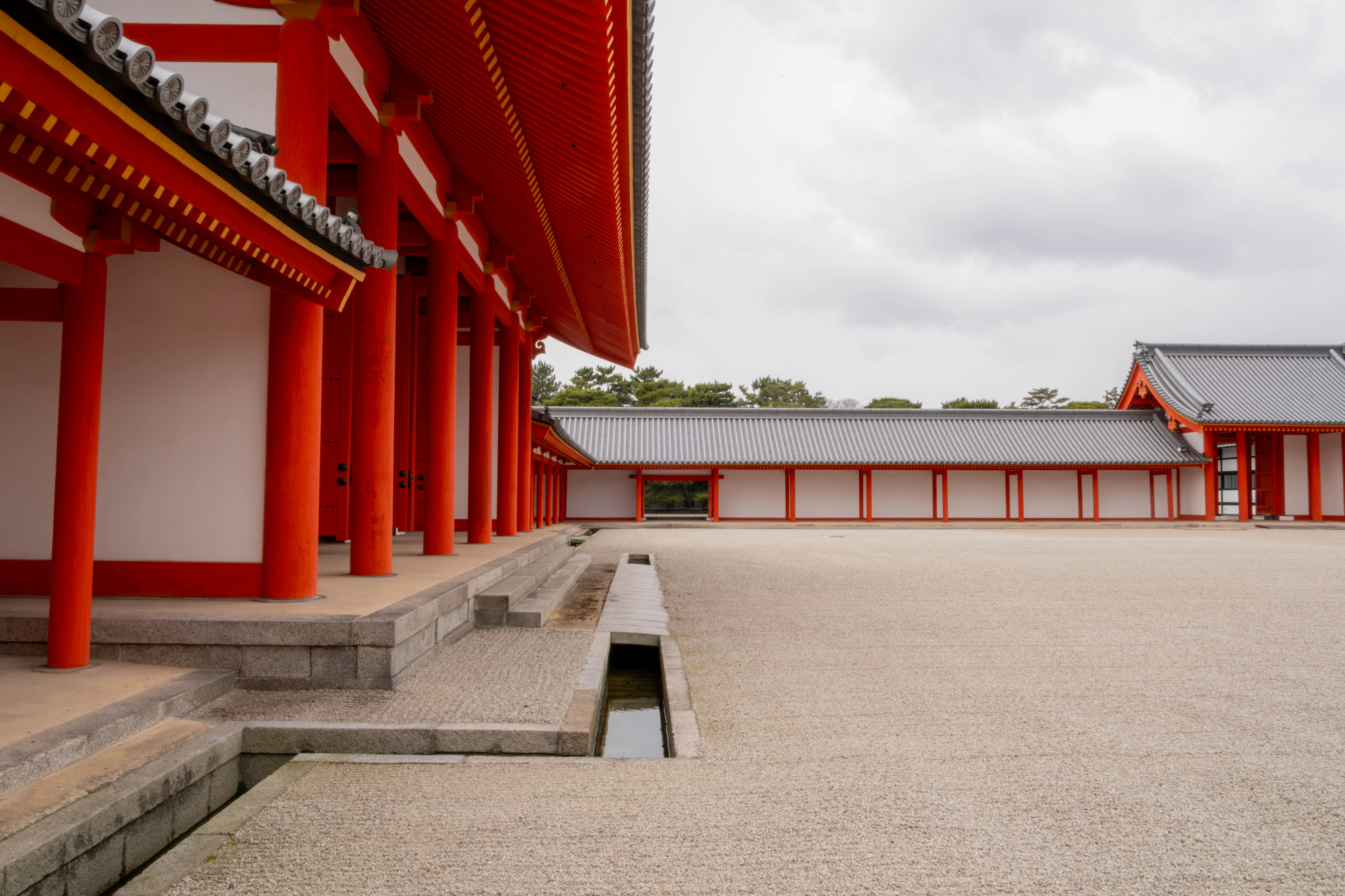 a building with red pillars and a small pond in front of it