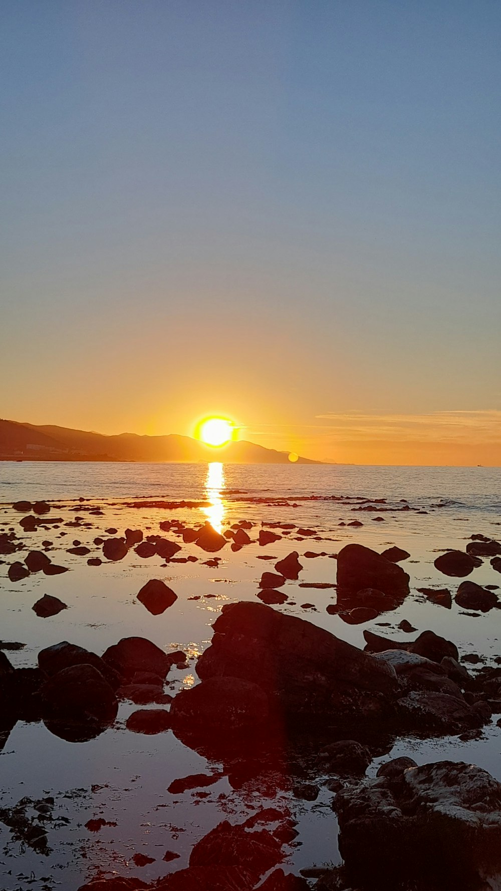 the sun setting over the ocean with rocks in the foreground