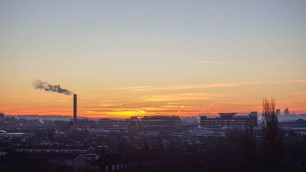 the sun is setting over a city with smoke stacks