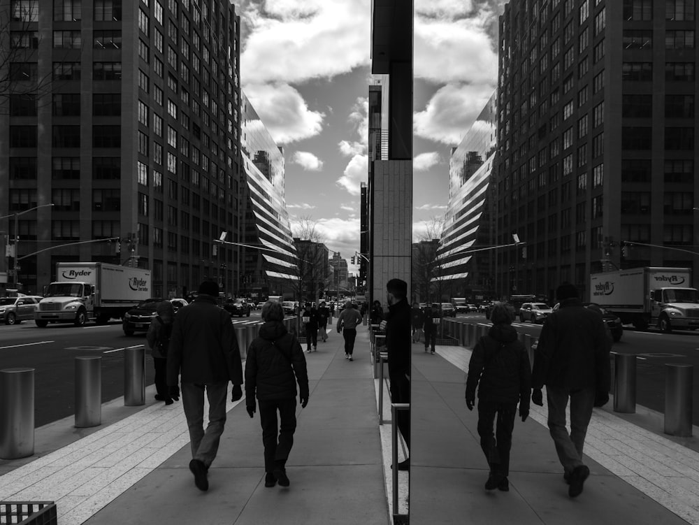 a group of people walking down a sidewalk next to tall buildings