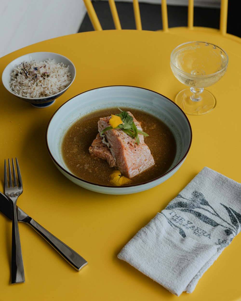 a bowl of soup and a glass of water on a yellow table