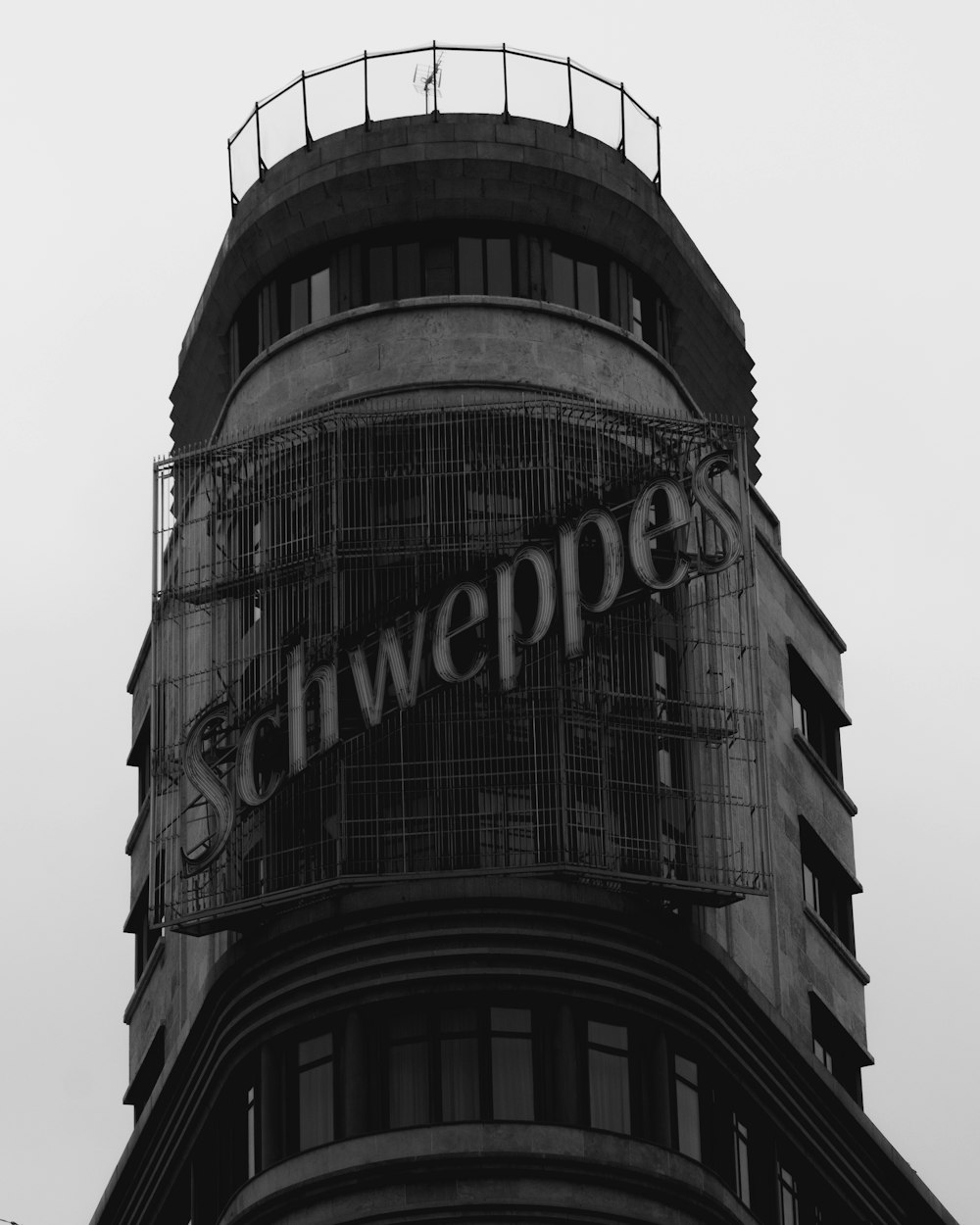 a black and white photo of a schweppes sign on a building