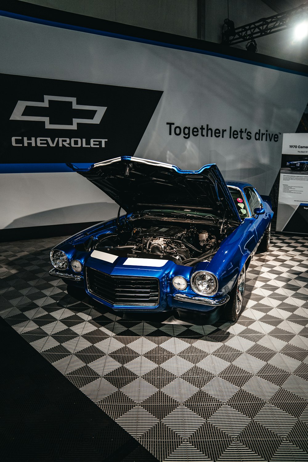 a blue car with its hood open on a checkered floor