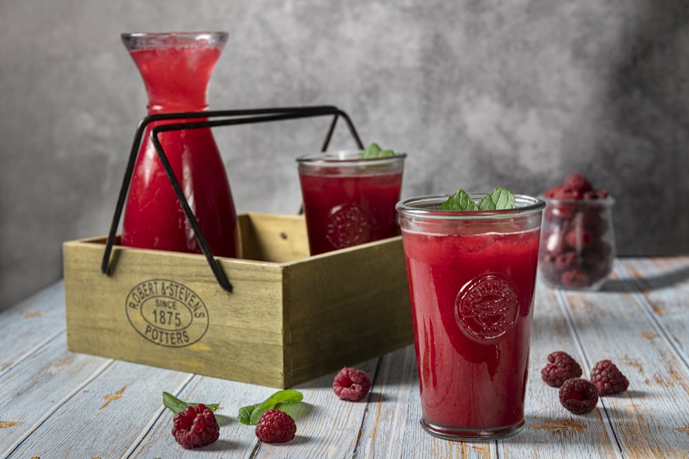 a glass of raspberry juice next to a wooden box of raspberries