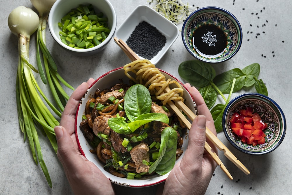 a person holding a bowl of food with chopsticks