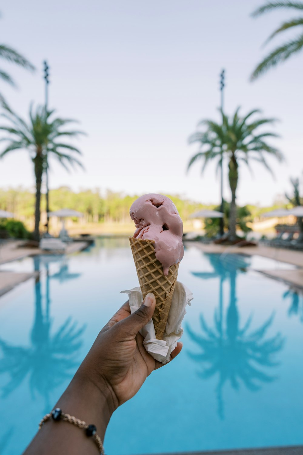 a person holding a pink ice cream cone in front of a swimming pool