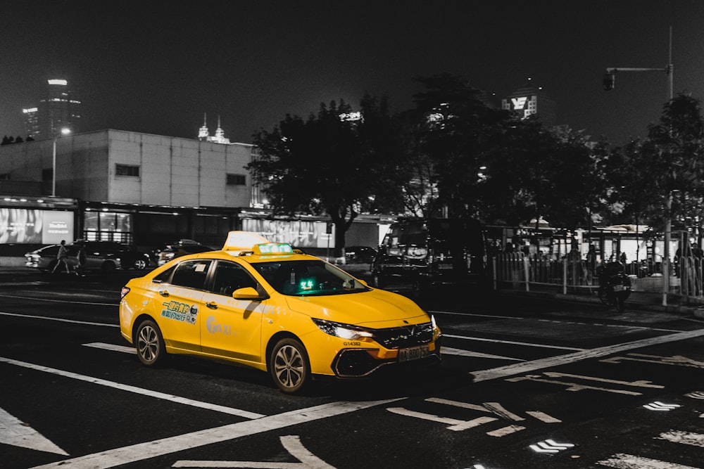 a yellow taxi cab driving down a street at night