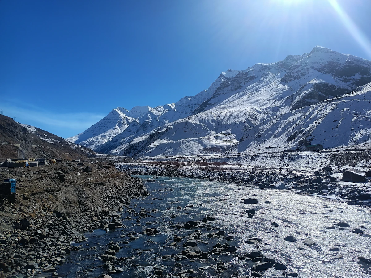 A wide braided river bed of grey gravel and snow running between steep snow-dusted high-altitude mountains