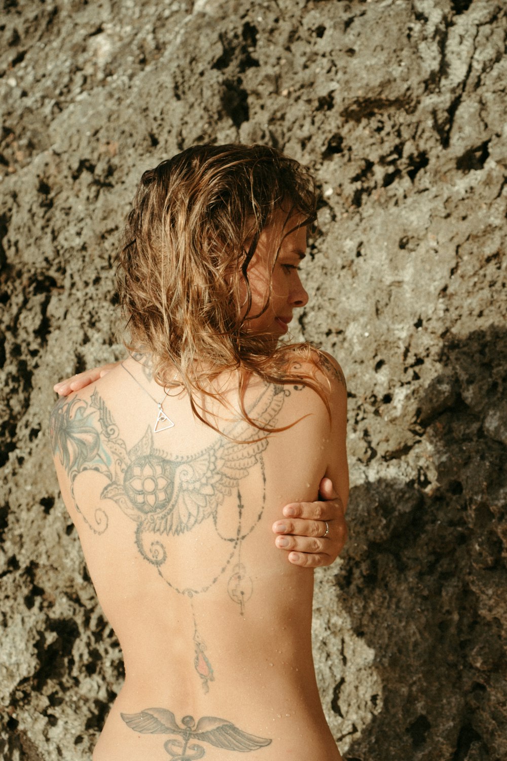 a woman with a tattoo on her back standing next to a rock