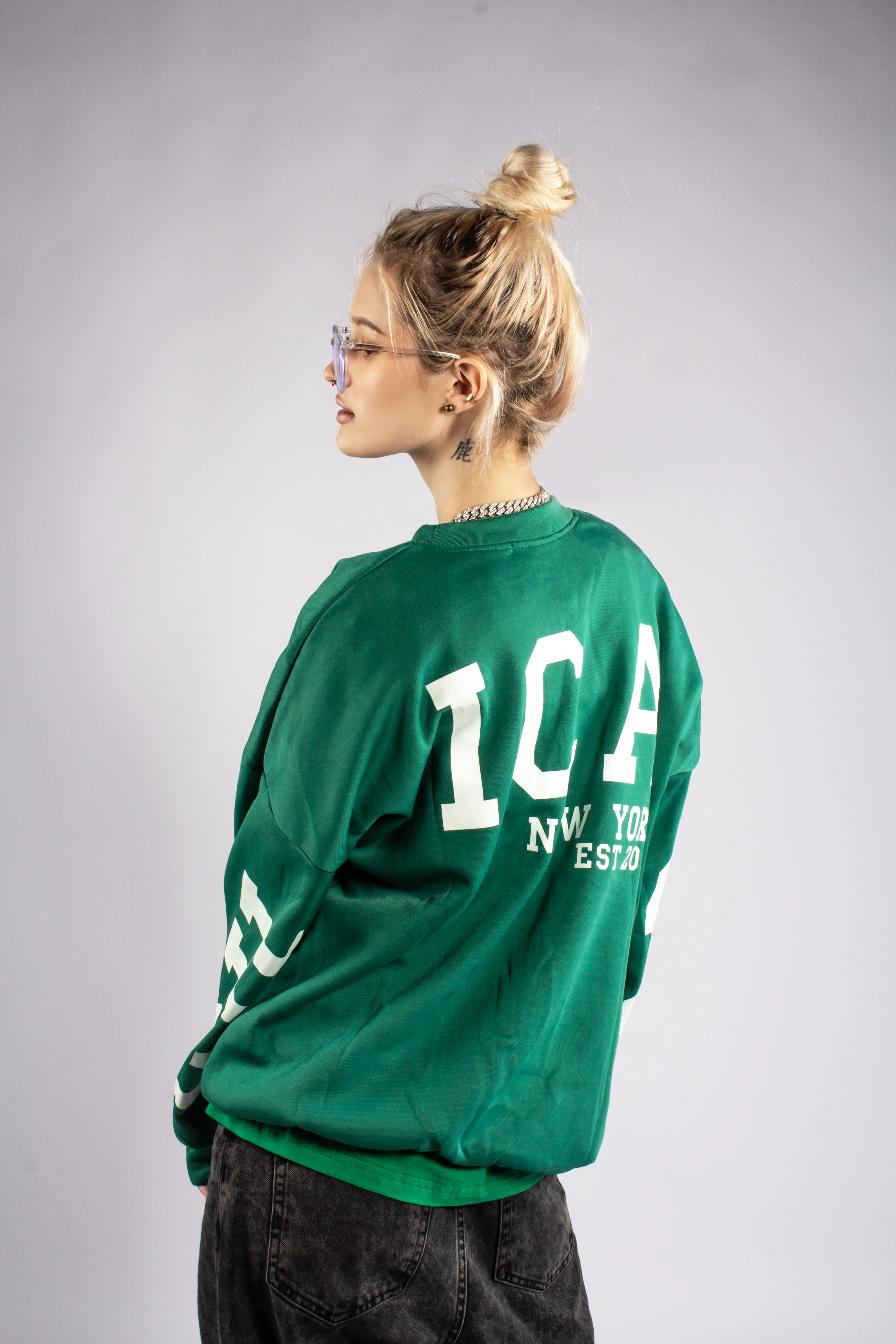 A student in an oversized green collegiate sweatshirt with white varsity lettering.