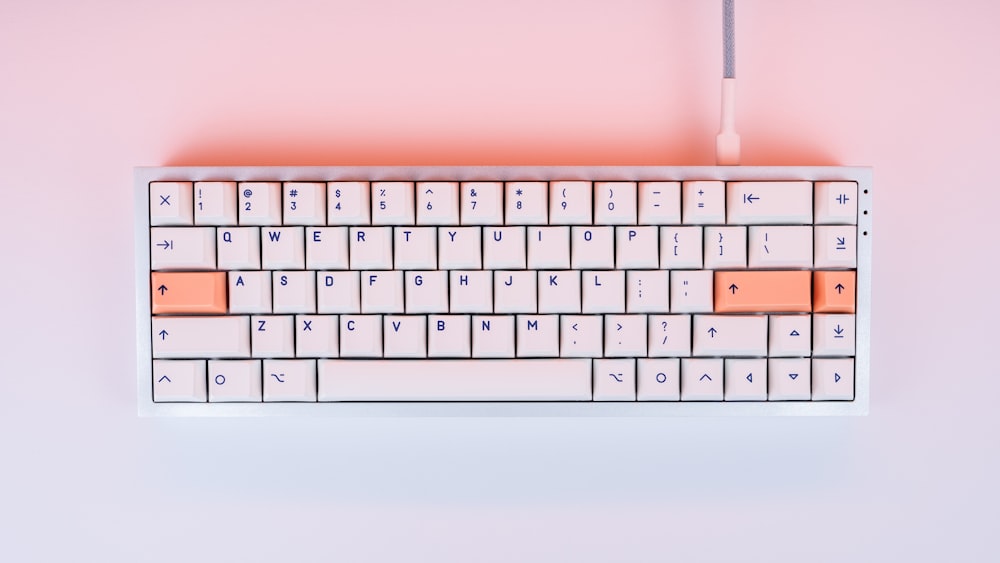 eine weiße und orangefarbene Tastatur auf rosa Hintergrund