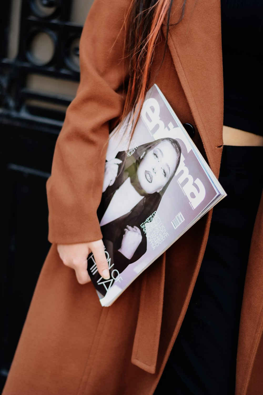 a woman in a brown coat holding a magazine