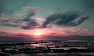 a couple of people standing on top of a beach under a cloudy sky