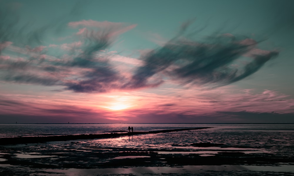 a couple of people standing on top of a beach under a cloudy sky