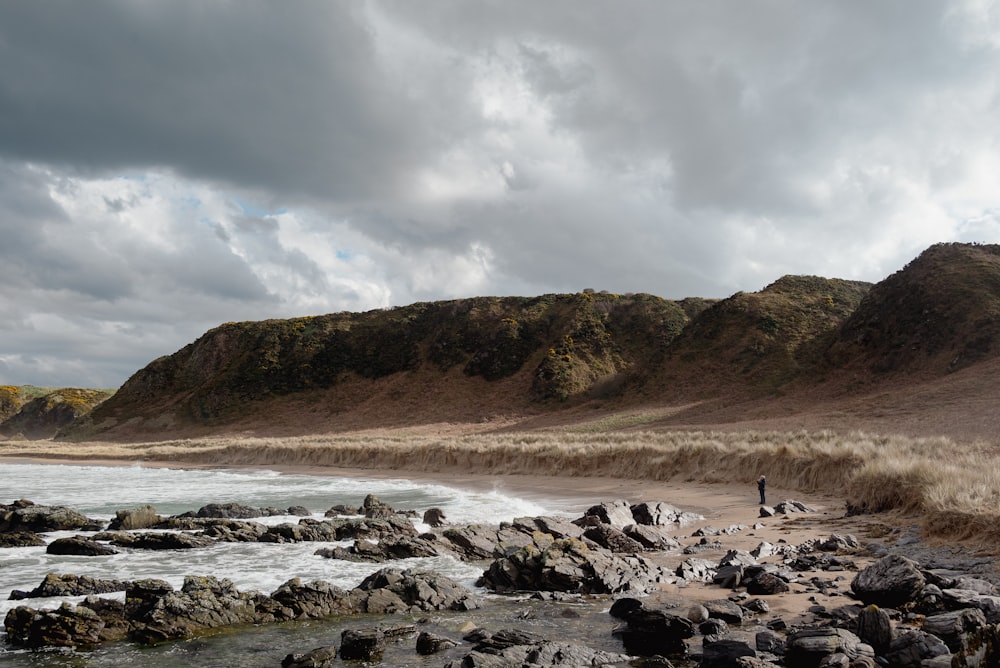 a man standing on a rocky beach next to a body of water