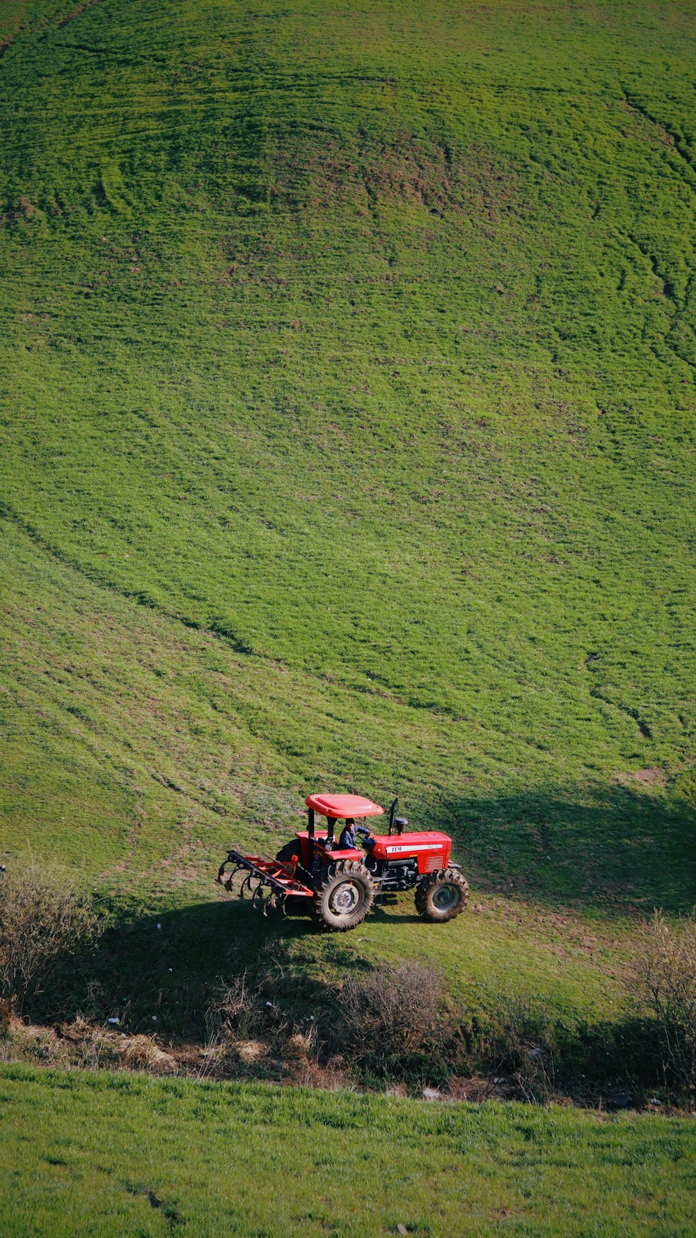a red tractor driving down a lush green hillside