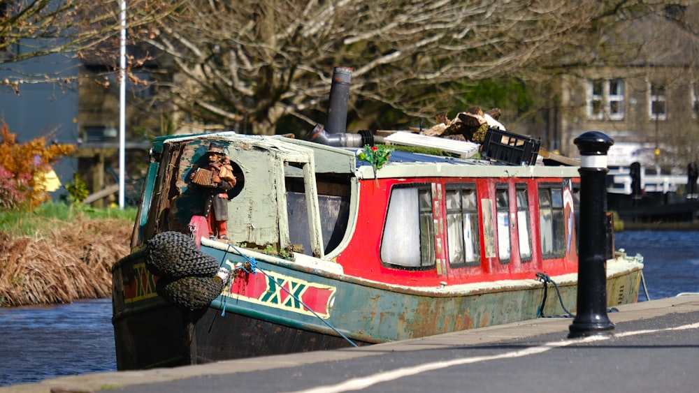 a red and green boat sitting on the side of a river