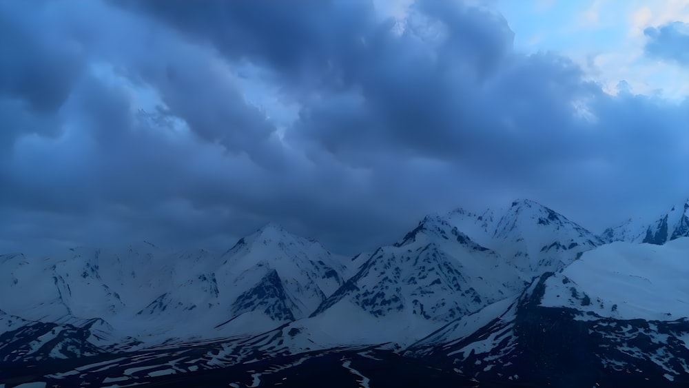 a mountain range covered in snow under a cloudy sky