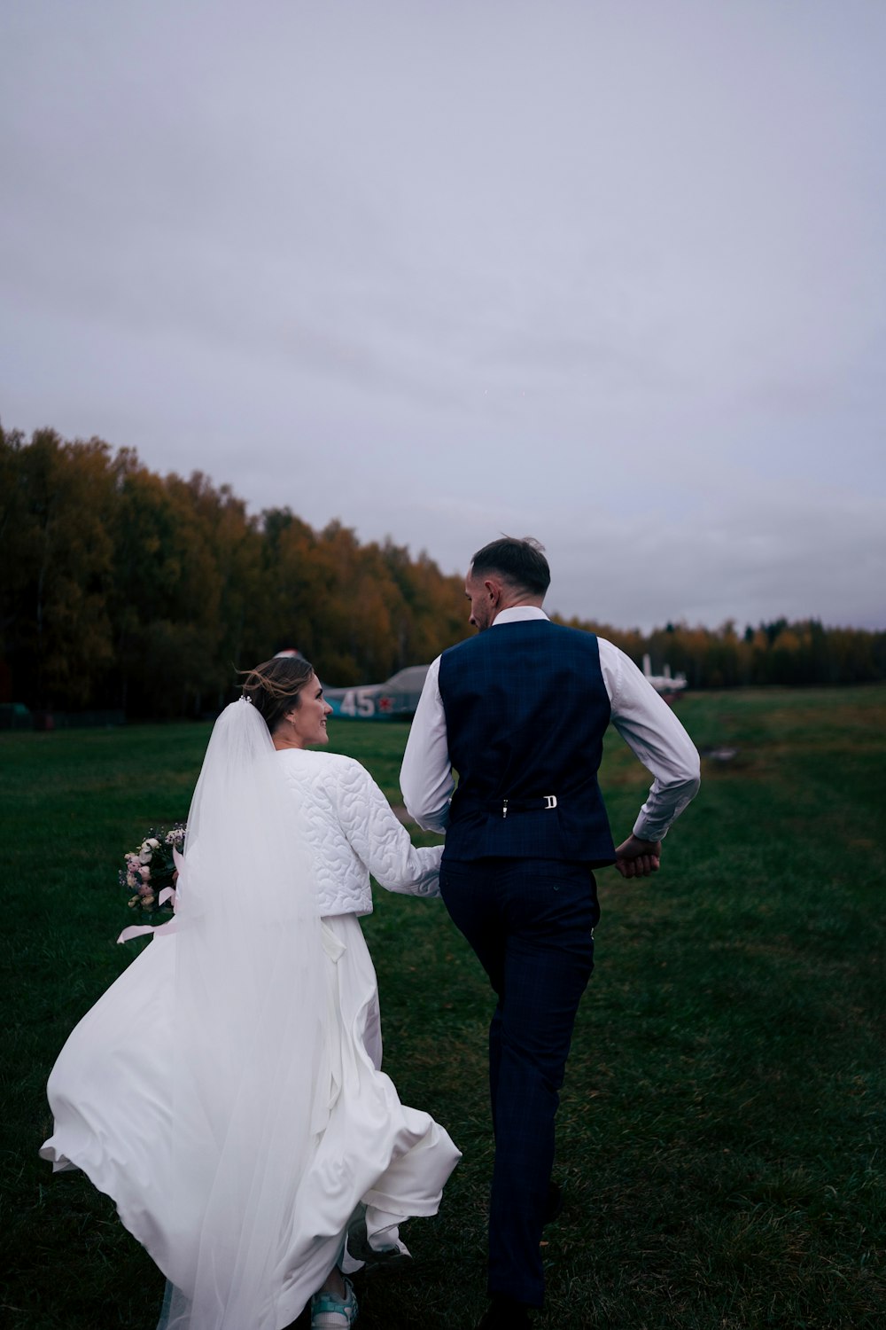 a bride and groom walking through a field