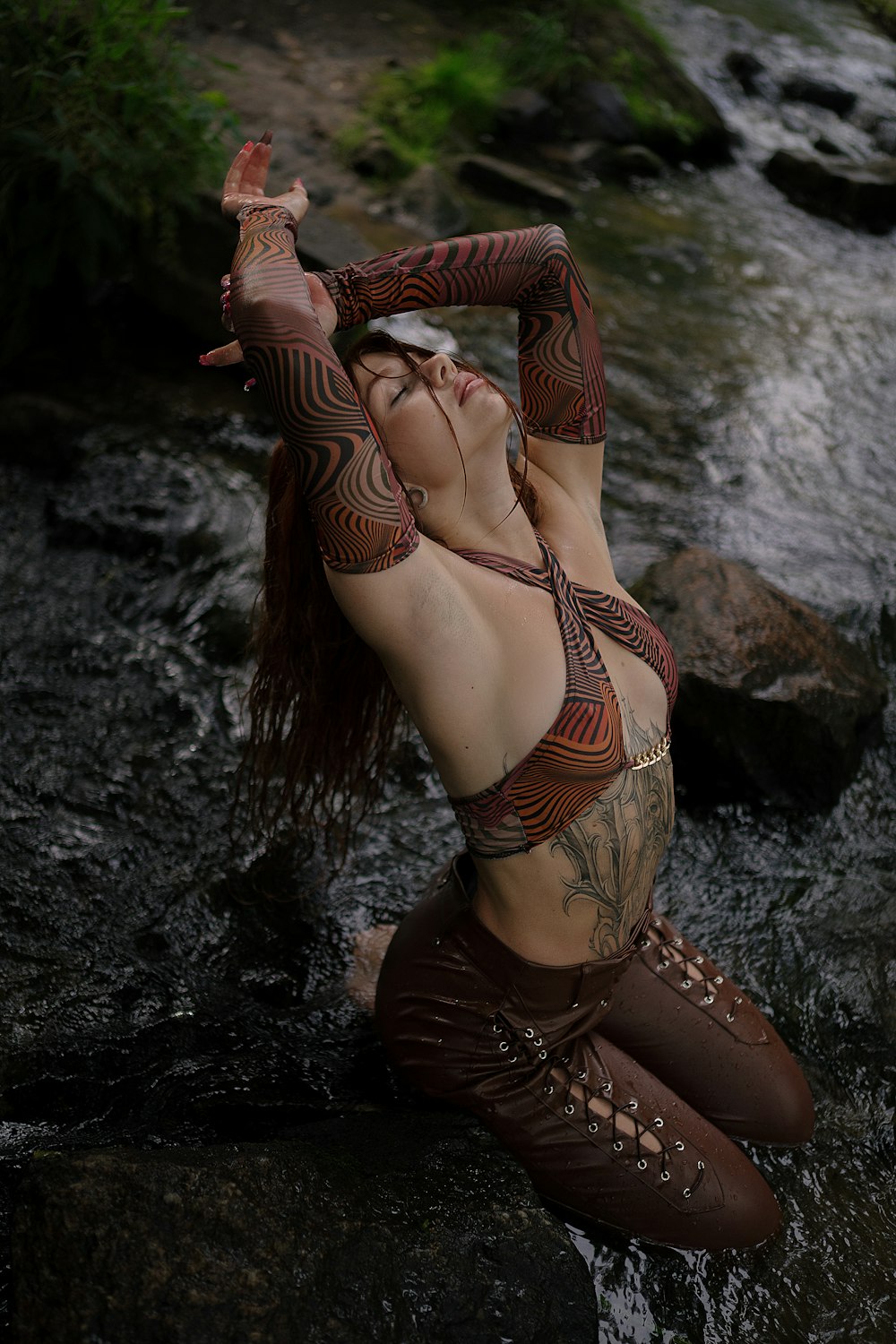 a beautiful woman in a bikini sitting on a rock next to a river