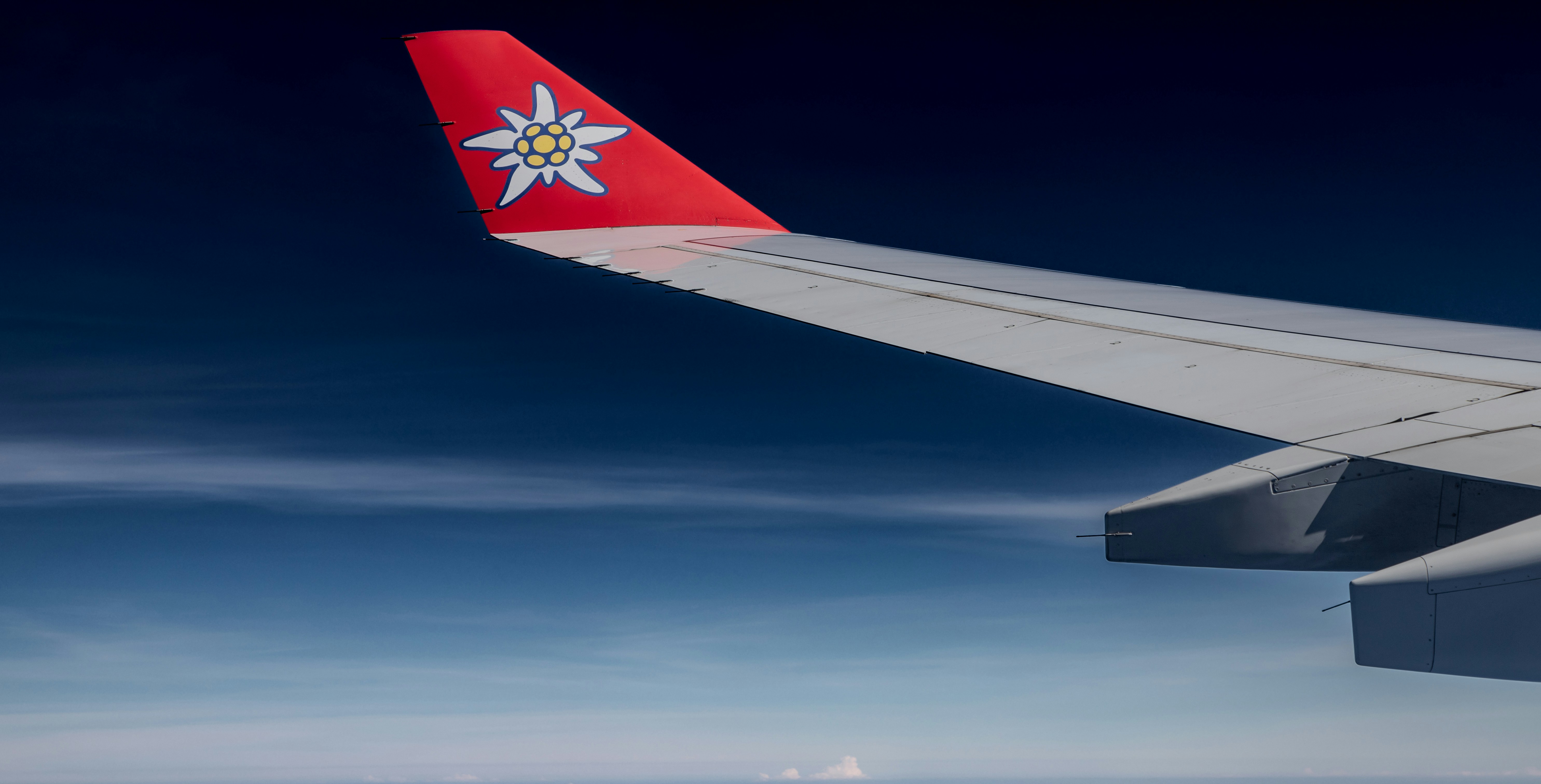 a view of the wing of an airplane in the sky, This image shows a clear view of an airplane wing against a bright blue sky, with a visible airline logo. The wing and engine indicate it
