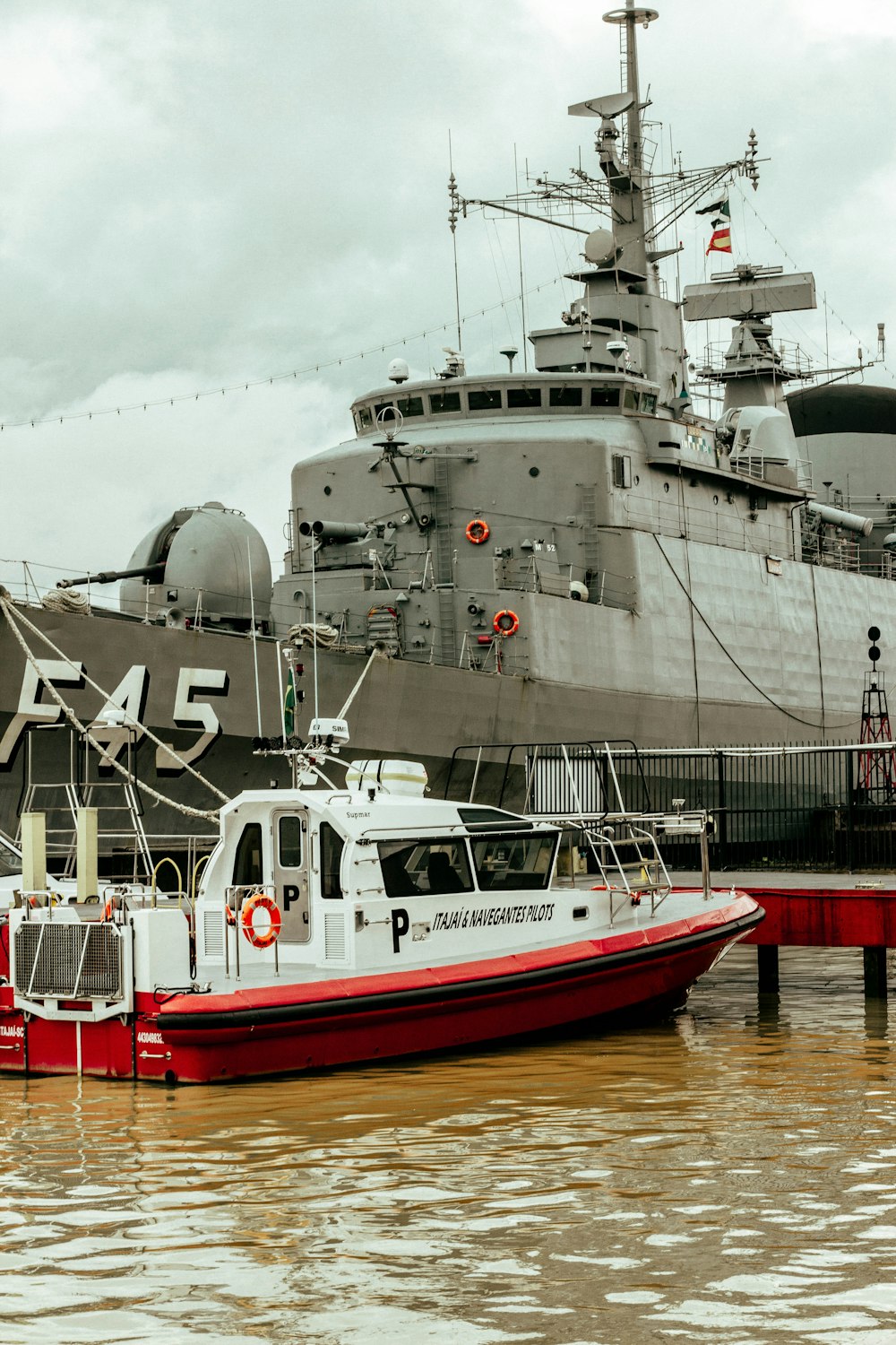 a red and white boat in the water next to a large ship