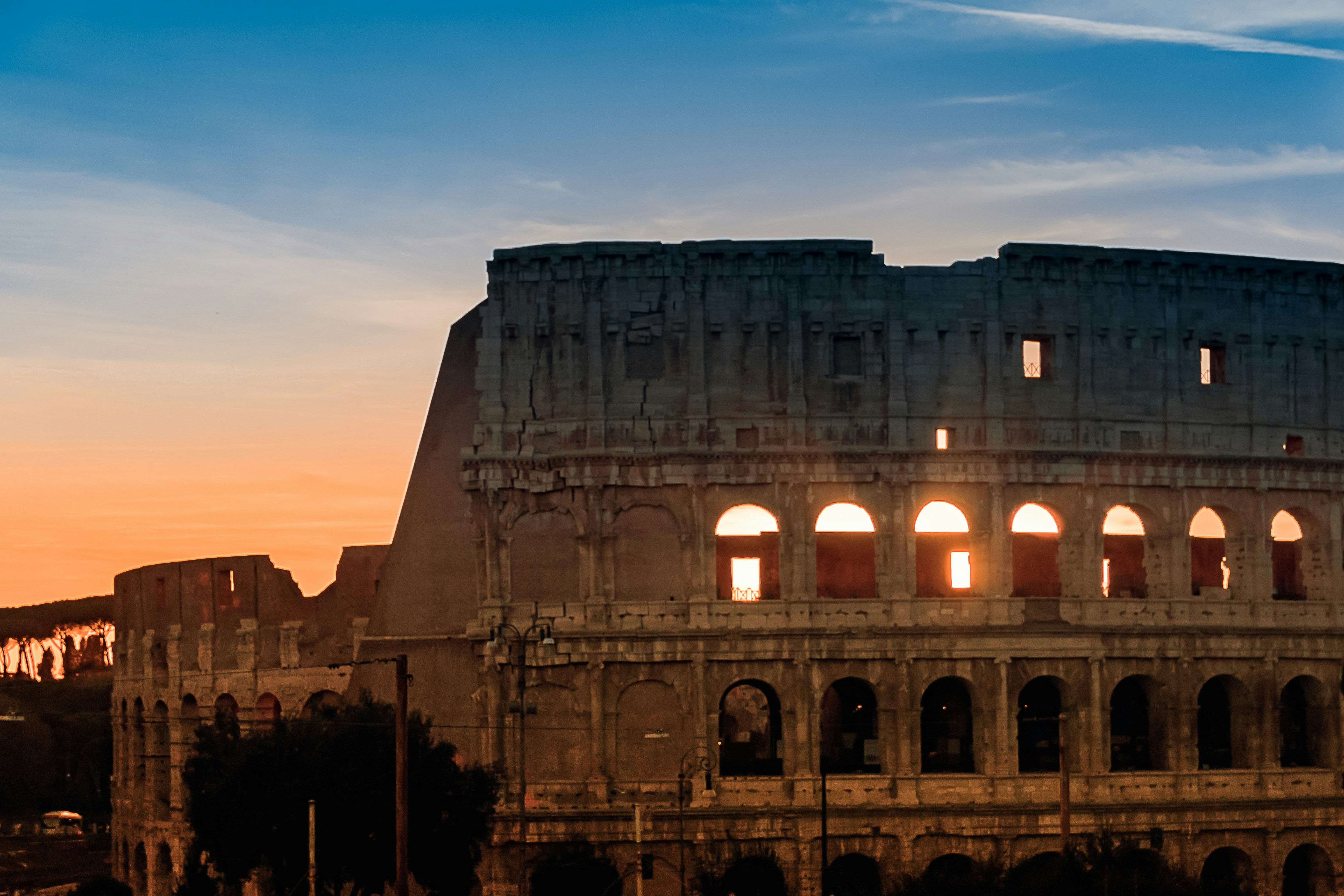 The iconic Colosseum in Rome at sunset, bathed in warm golden light, with a few tourists in the foreground - last minute holiday europe