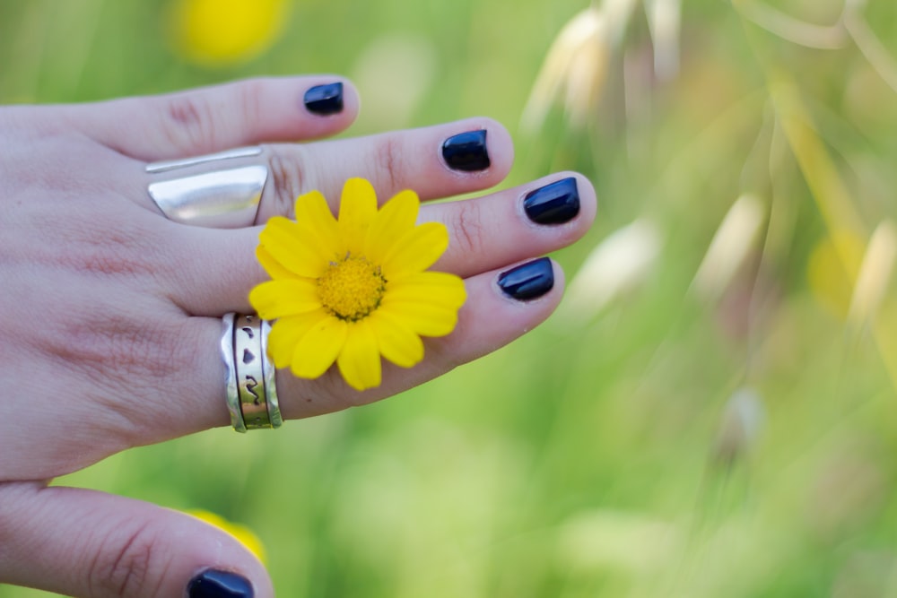 a woman's hand with a ring and a yellow flower