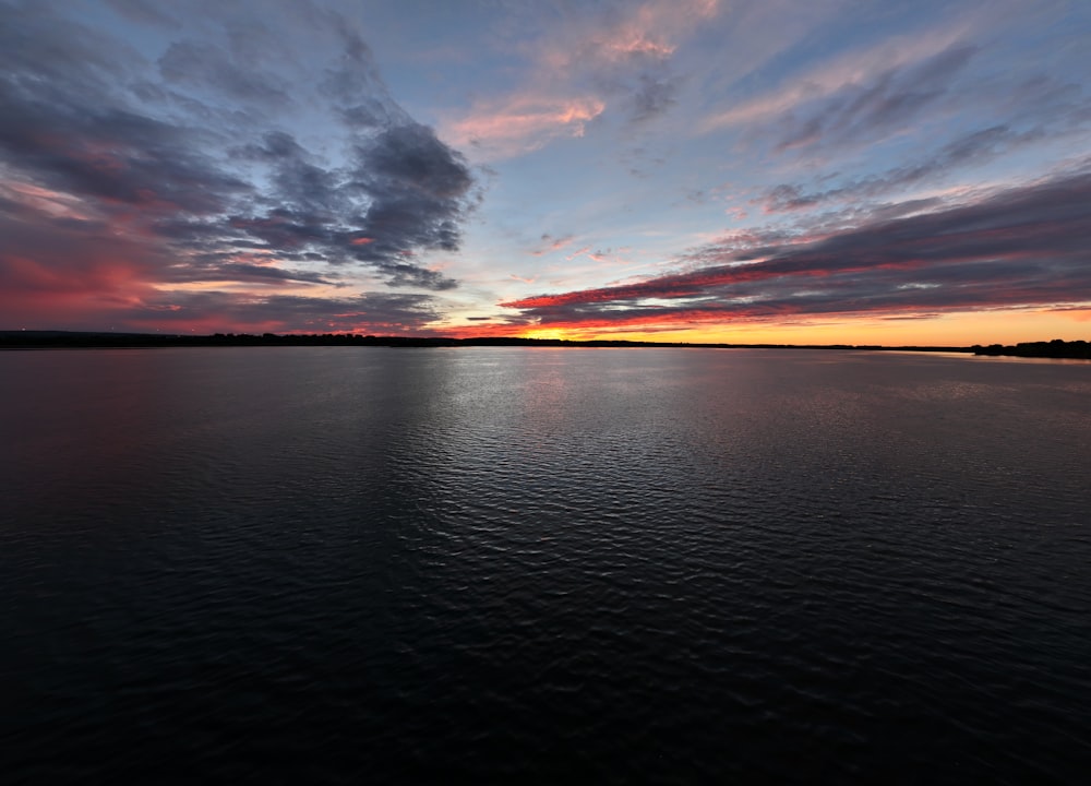 the sun is setting over the water with clouds in the sky