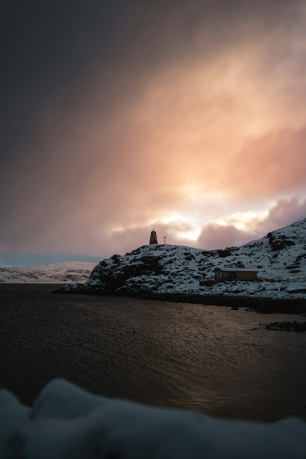 a lighthouse on top of a snowy hill under a cloudy sky