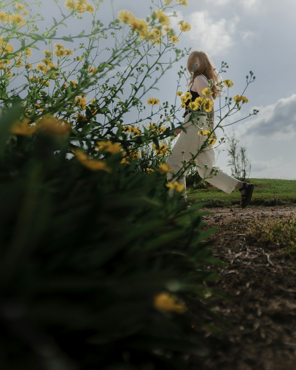 a woman walking through a field of yellow flowers
