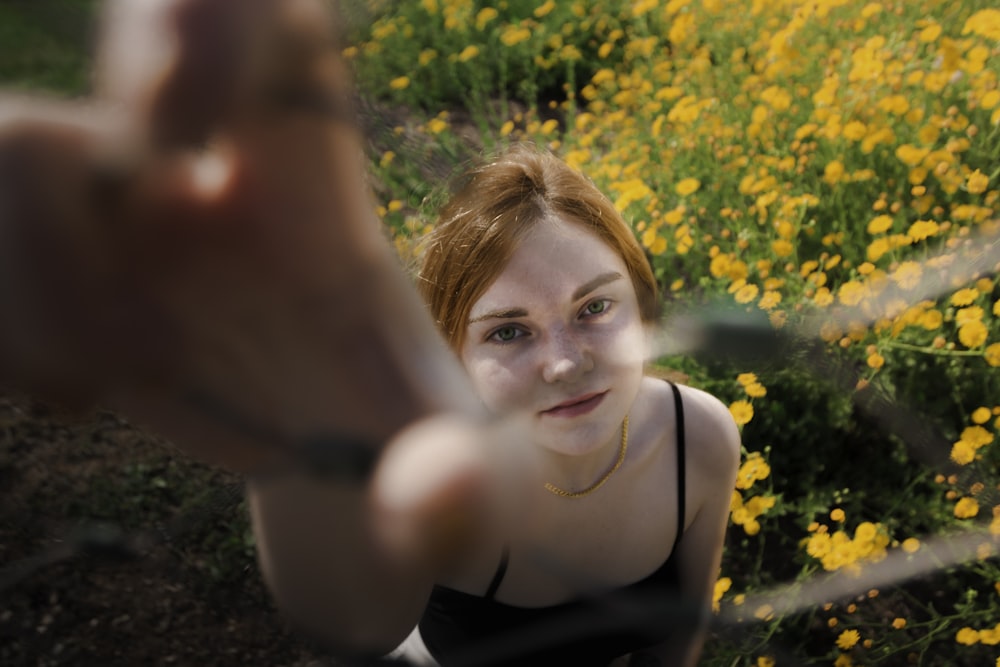 a woman in a black tank top standing in a field of yellow flowers
