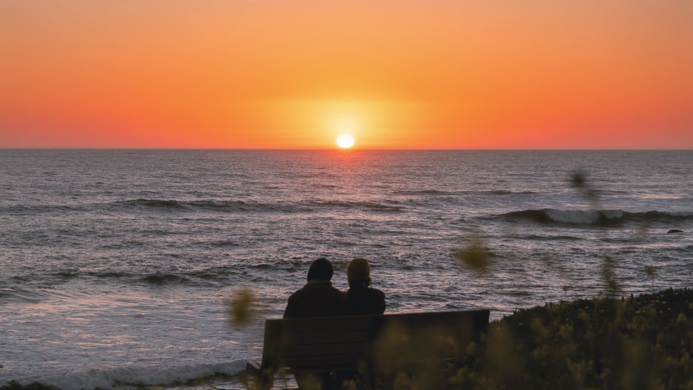 two people sitting on a bench watching the sunset