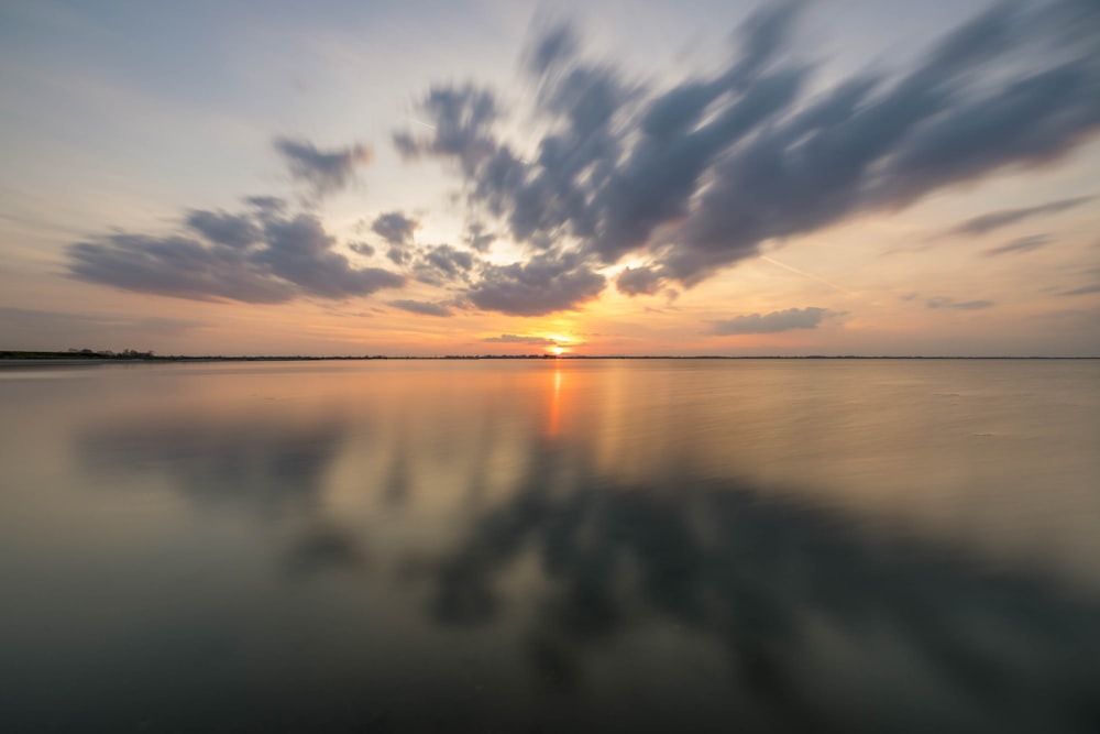 the sun is setting over the water with clouds in the sky