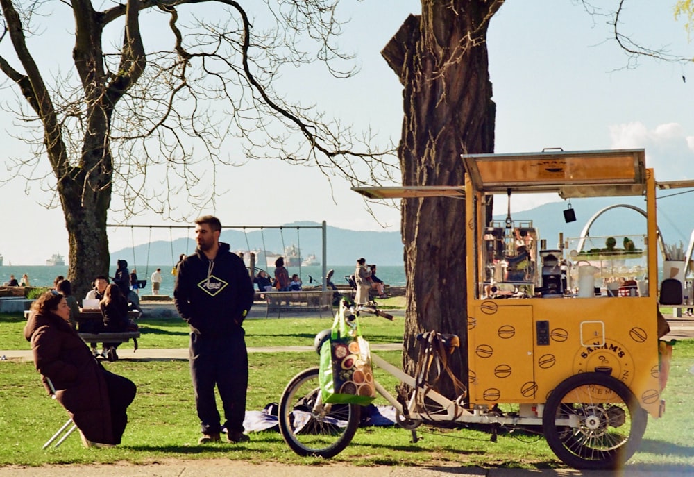 a man standing next to a yellow truck parked next to a tree