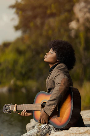 a woman sitting on a rock playing a guitar