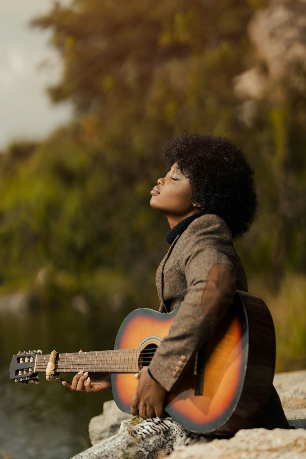 a woman sitting on a rock playing a guitar