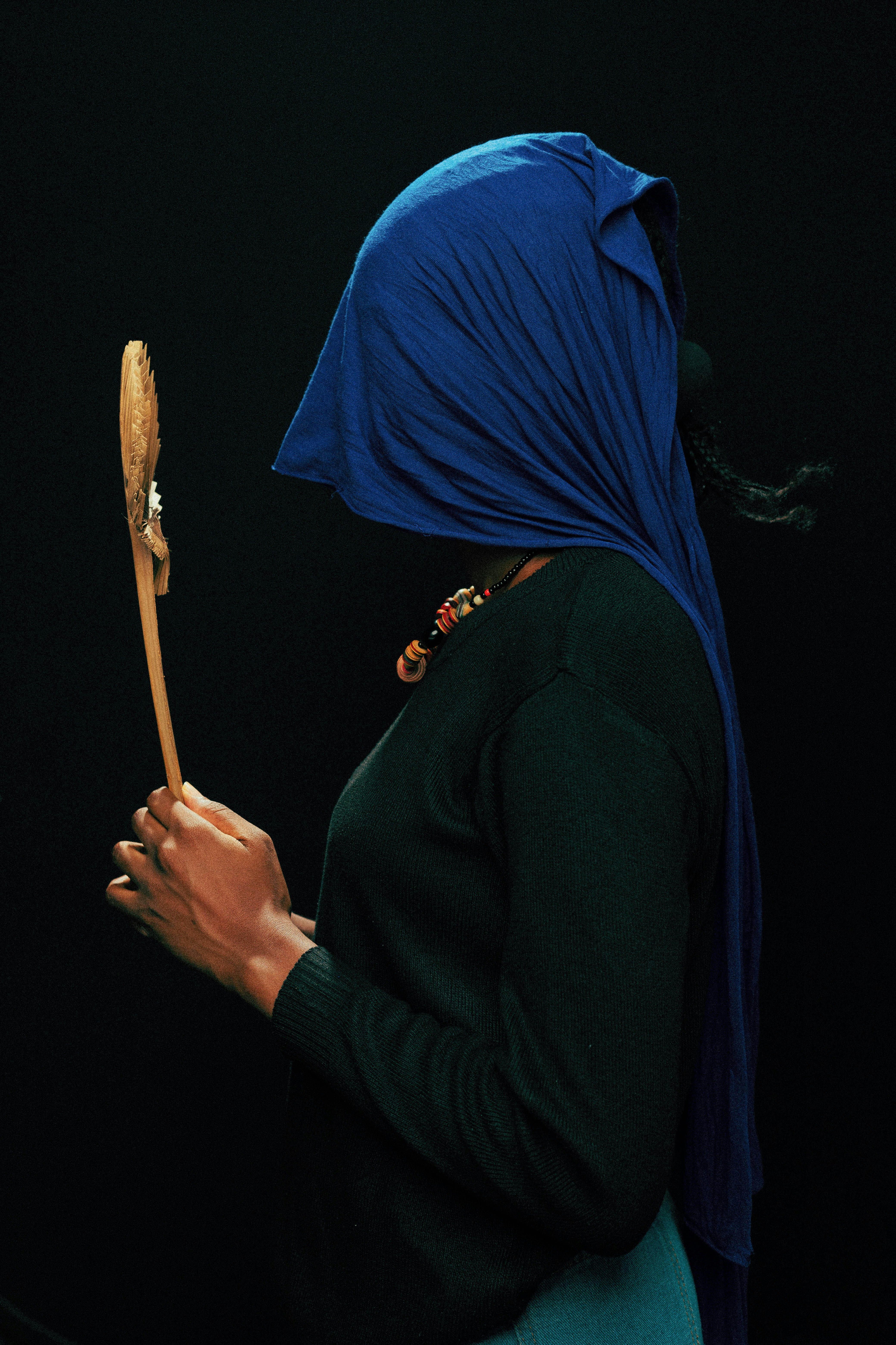 a woman with a blue head covering holding a wooden stick