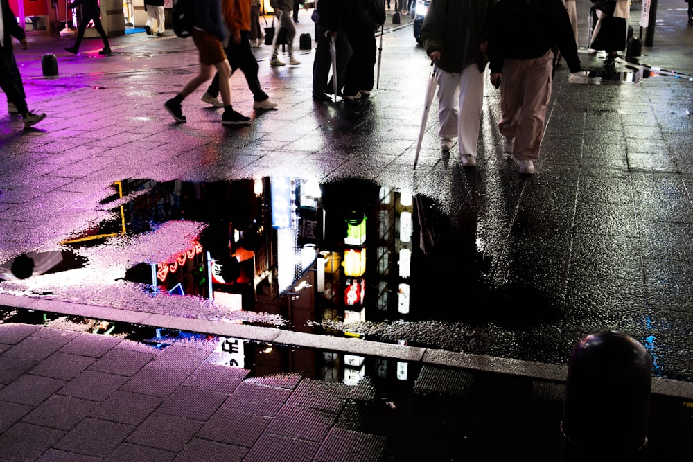 a group of people walking down a street next to a puddle