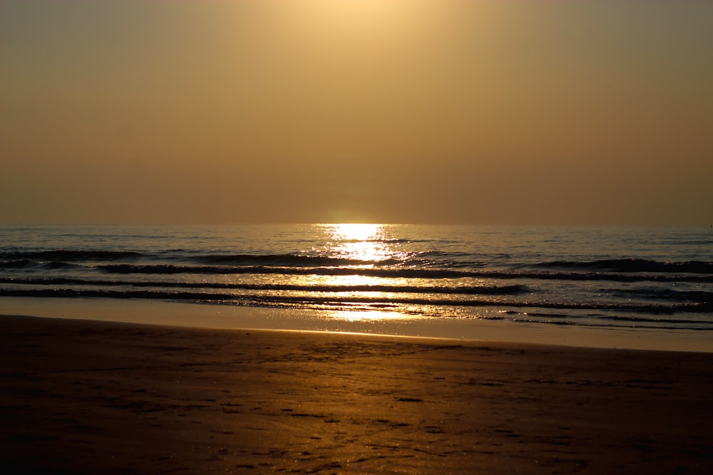 the sun is setting over the ocean on the beach