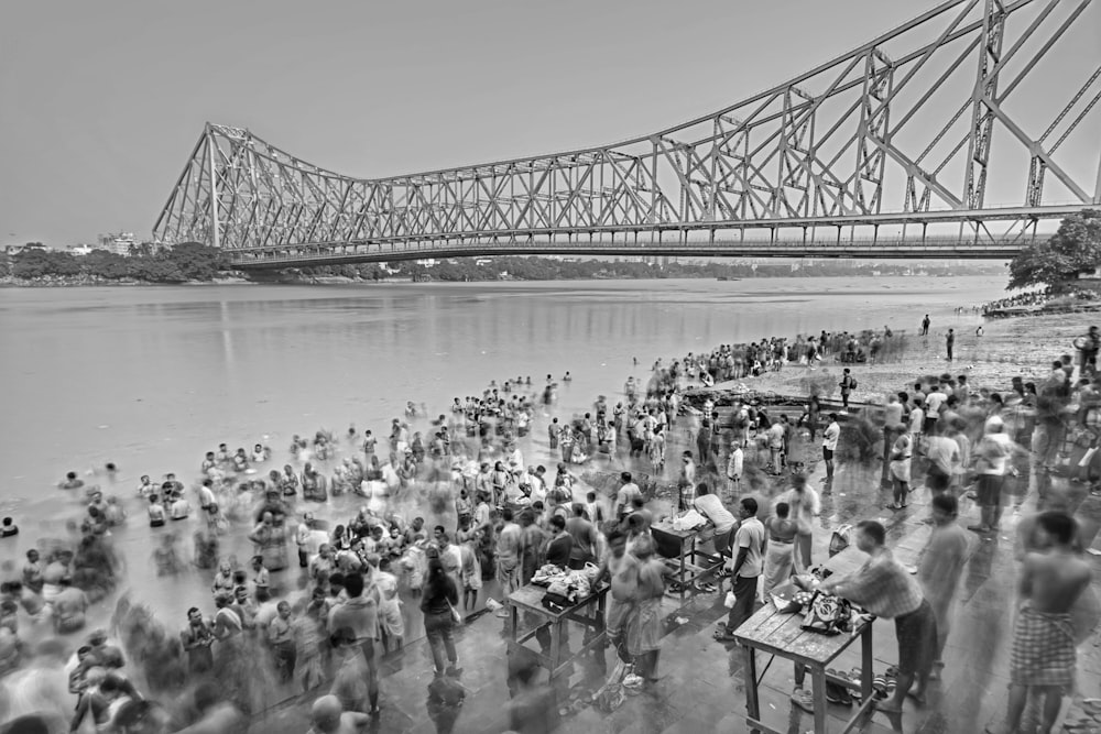 uma multidão de pessoas em pé em uma praia ao lado de uma ponte