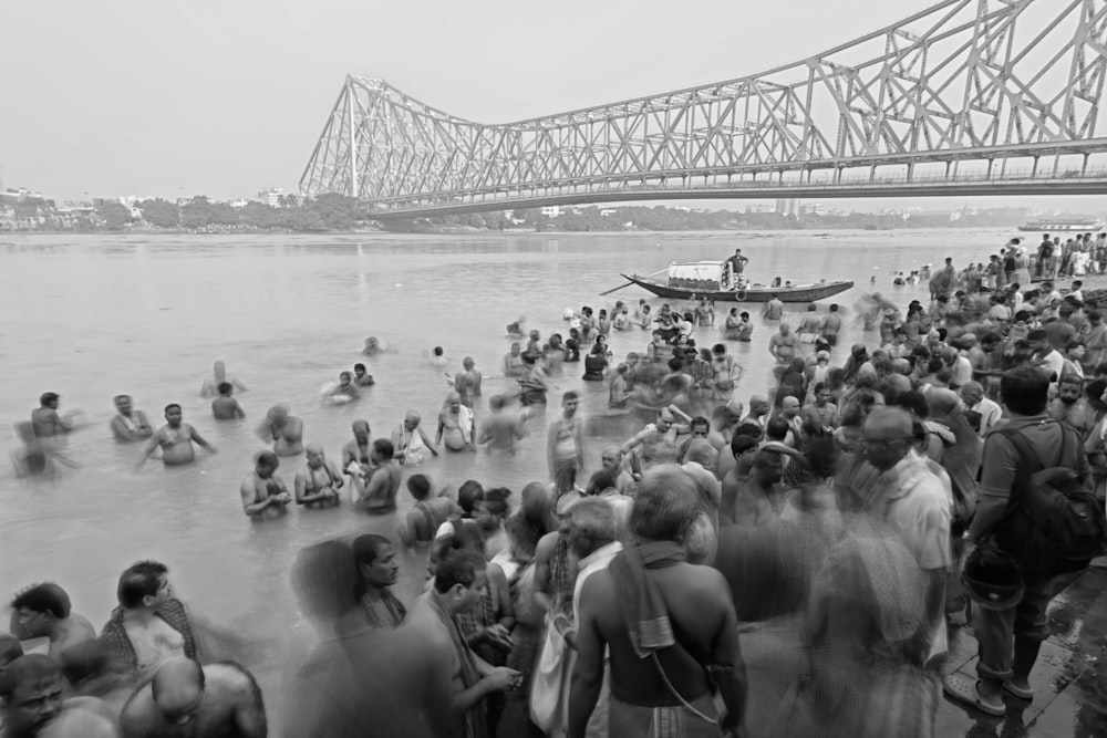 a crowd of people standing in the water near a bridge
