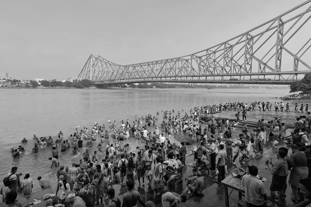 a large group of people standing in the water near a bridge