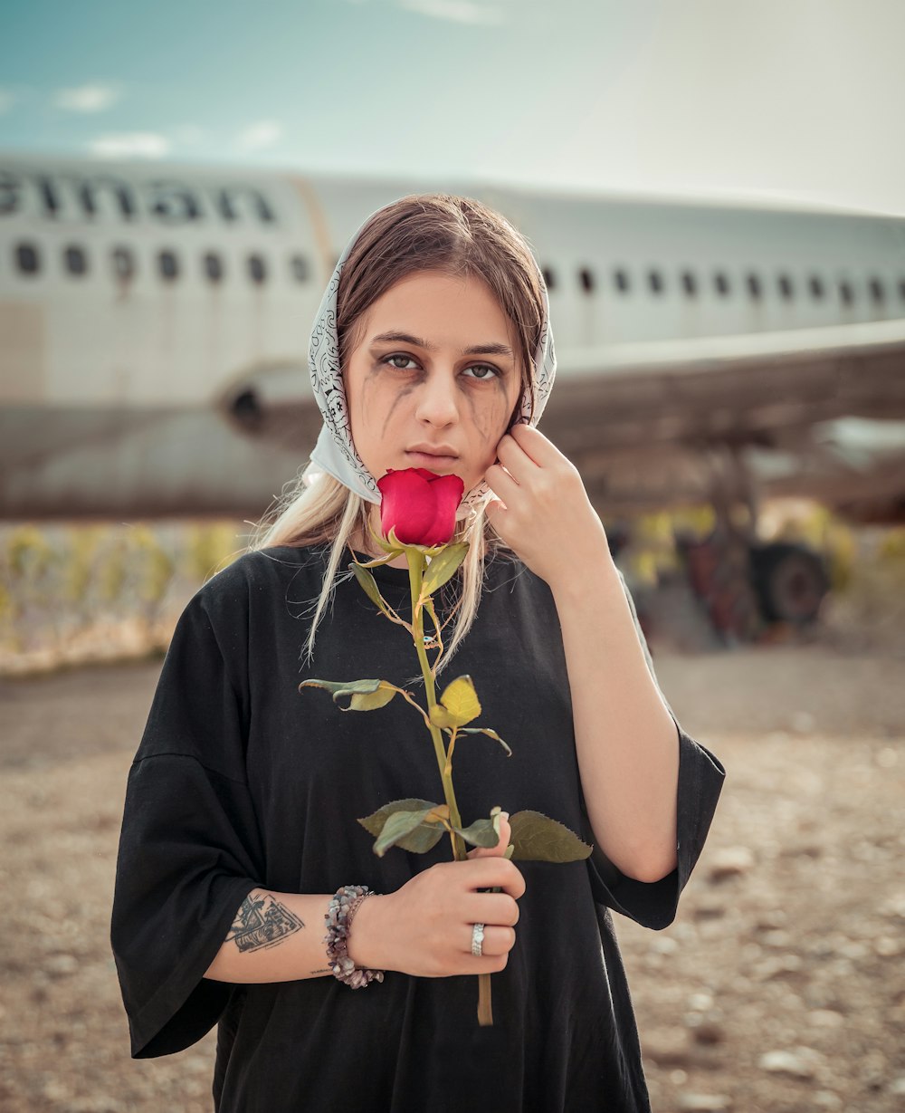 a woman holding a rose in front of an airplane