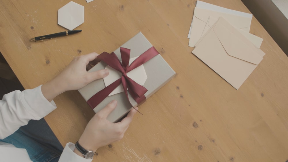 a person opening a gift box with a red ribbon