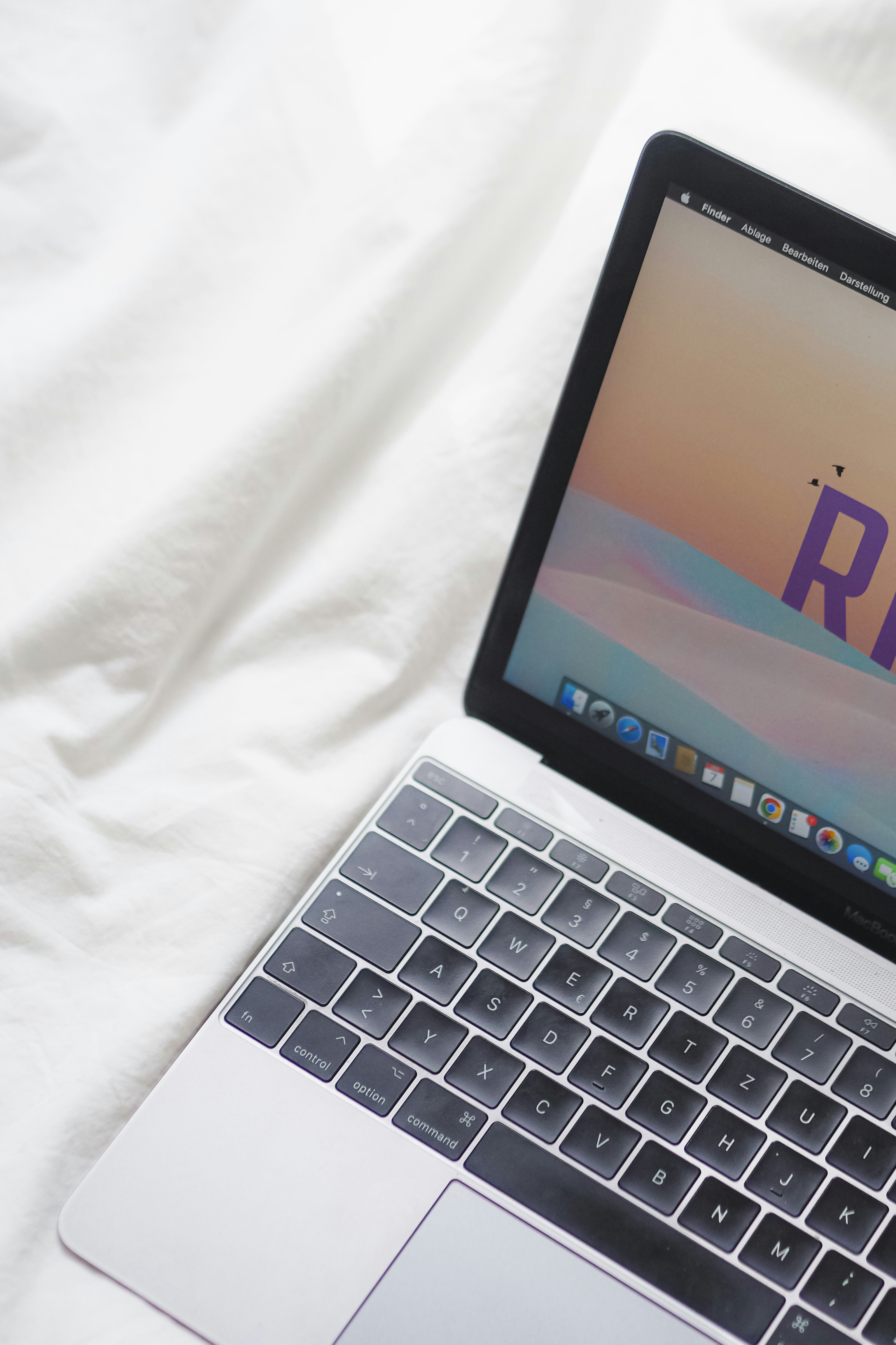 komputer laptop terbuka yang duduk di atas tempat tidur putih