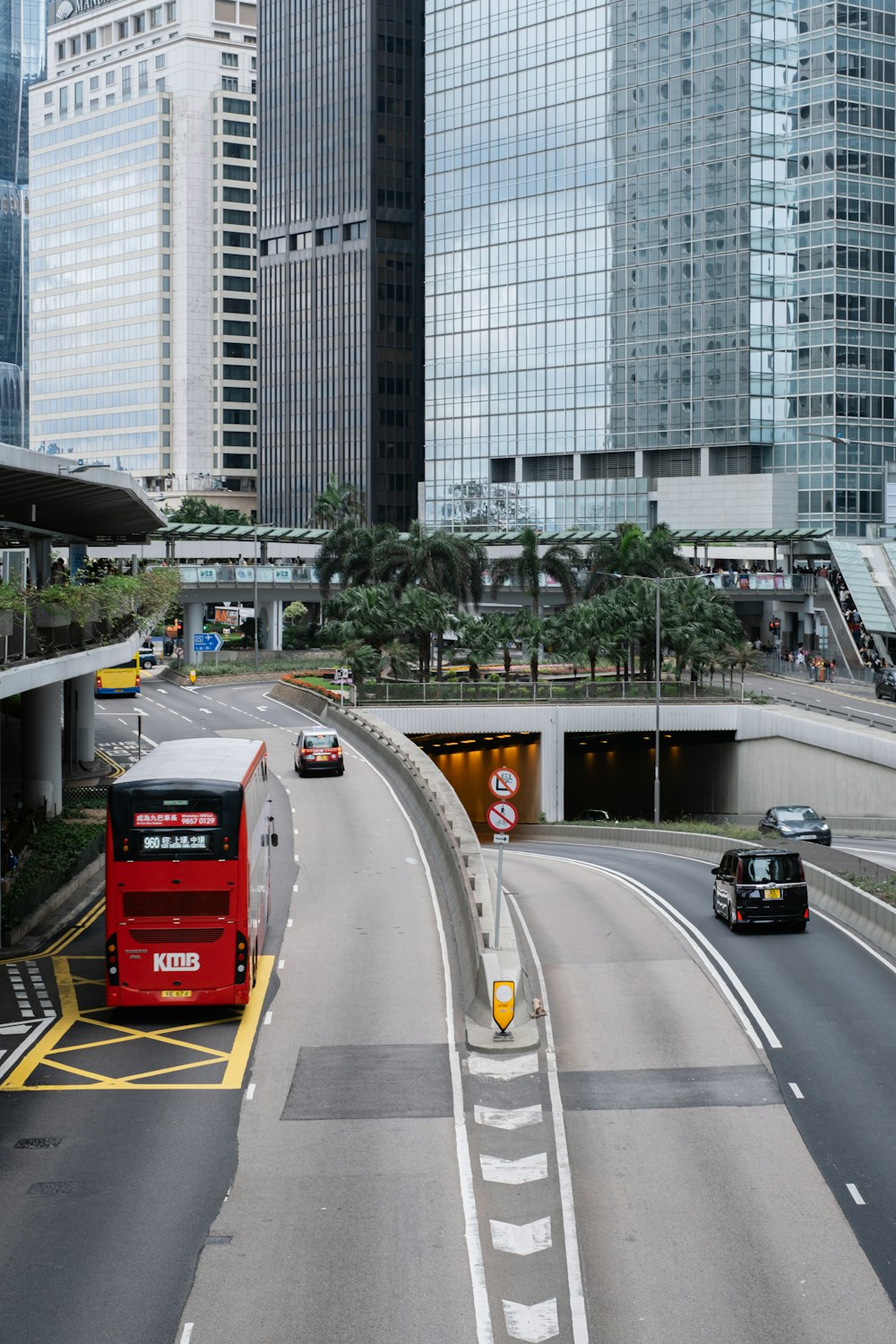 a red double decker bus driving down a street next to tall buildings