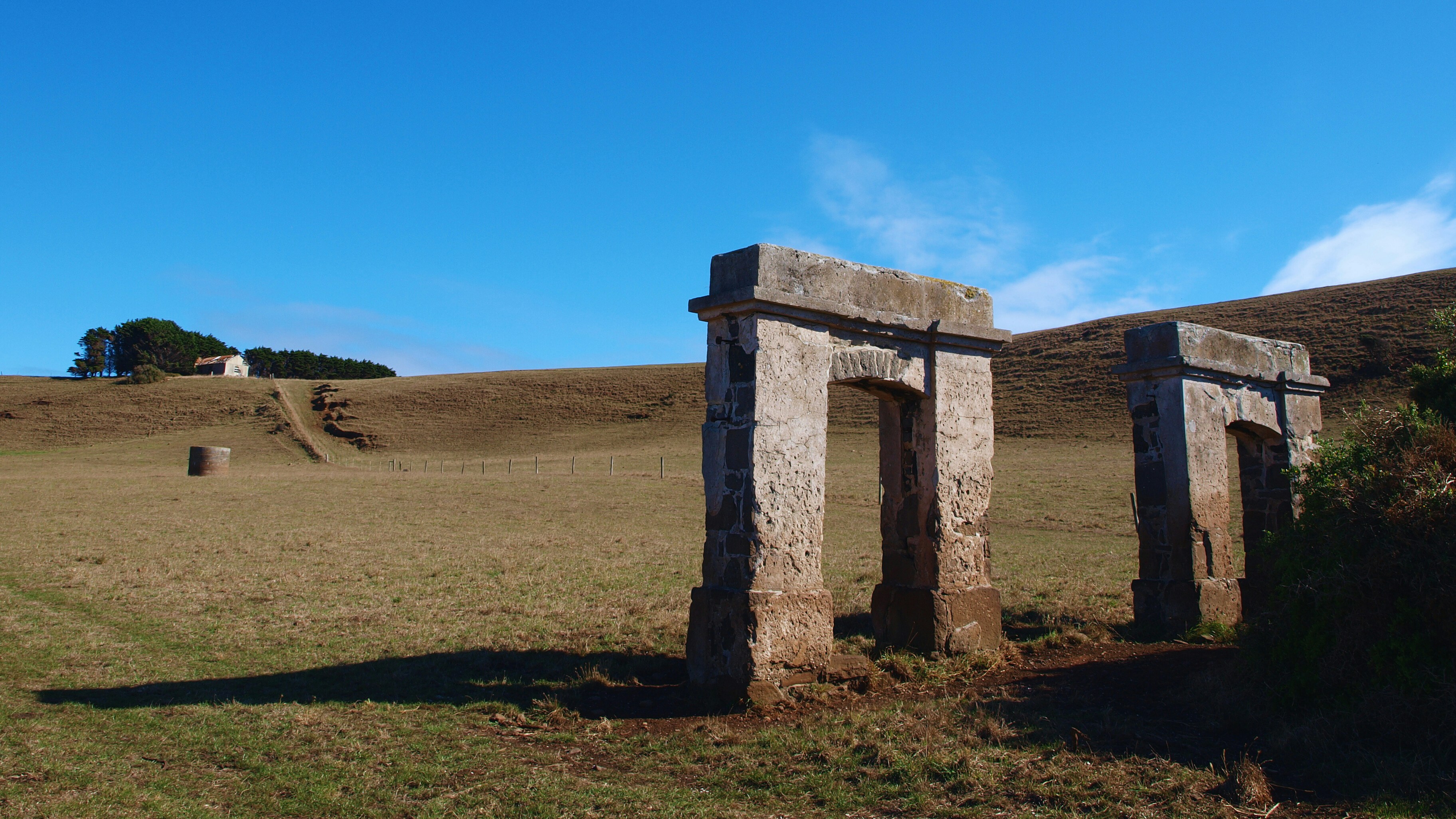 two stone pillars in a grassy field with a hill in the background